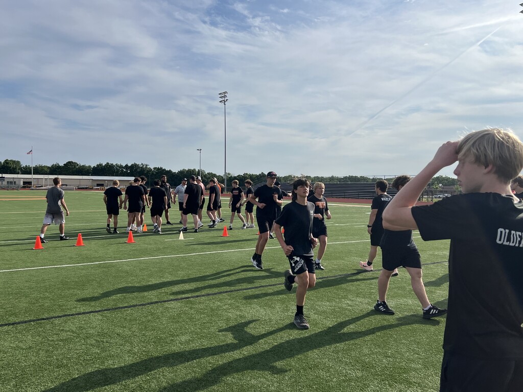 Multiple individuals in athletic wear on a field with orange cones, one looking up at the sky.
