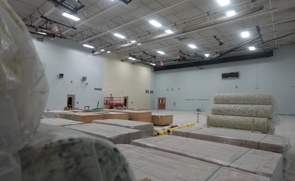 A construction site with several wooden boxes and carpet rolls in a large, empty room with fluorescent lights.