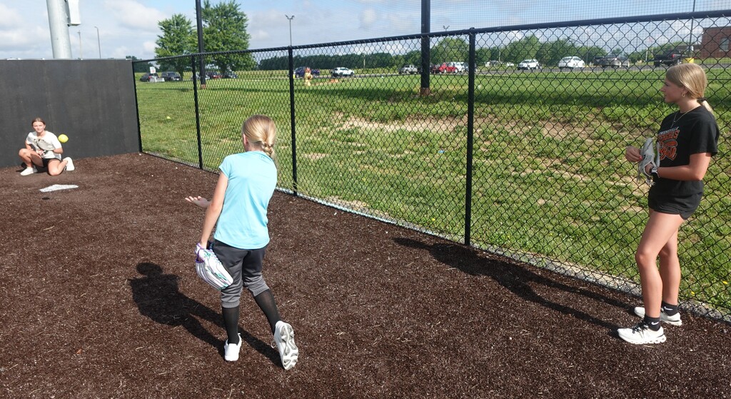 Two individuals are playing catch on a field with a chain-link fence, one holding a ball.