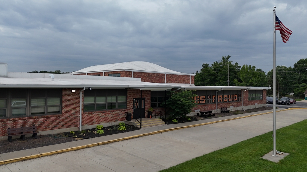 A brick building with a white roof, windows, and a sign reading "GES Group." An American flag flies on a pole.