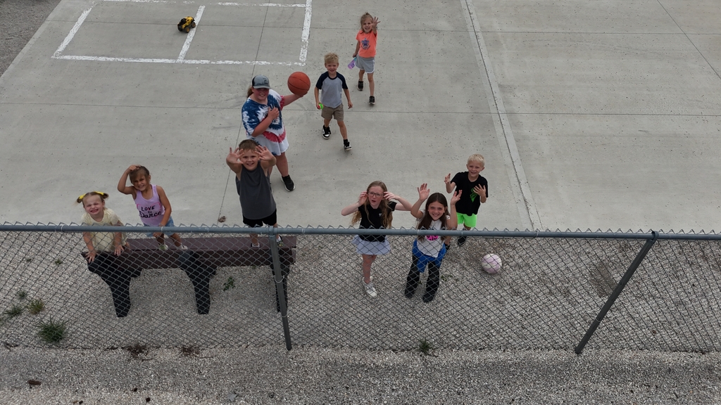 Children playing basketball and soccer in a paved outdoor area with a chain-link fence.