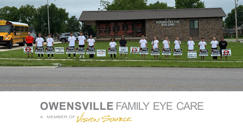 People in white shirts stand in a line, holding signs. A building is in the background. Text reads "Owensville Family Eye Care".