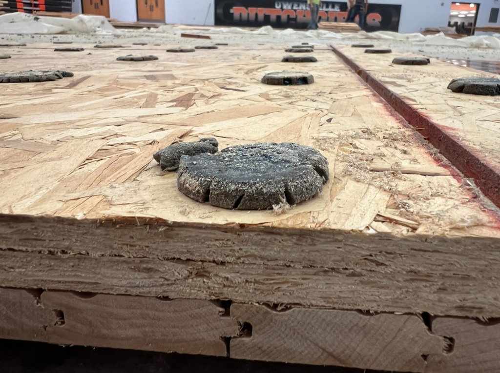 Wooden surface with multiple circular holes. A large round piece of wood sits on the surface.