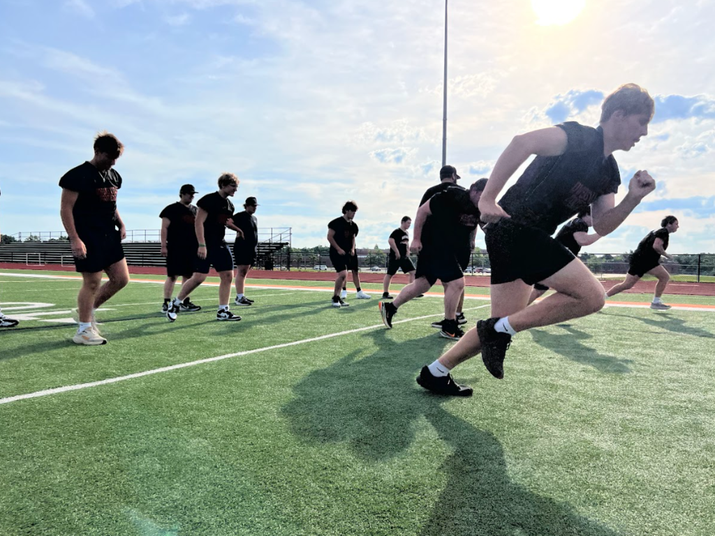 A group of people dressed in black athletic wear run on a field with white lines.