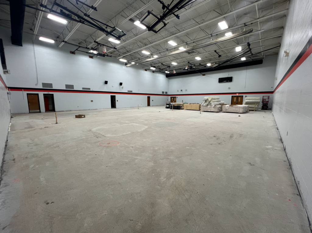 An empty large room under construction with concrete floor, white walls, and red stripes at the top.