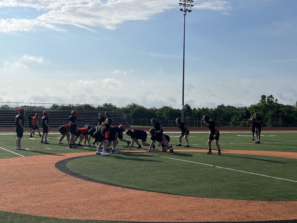 Several people in sports gear practicing on a football field with a light pole in the background.