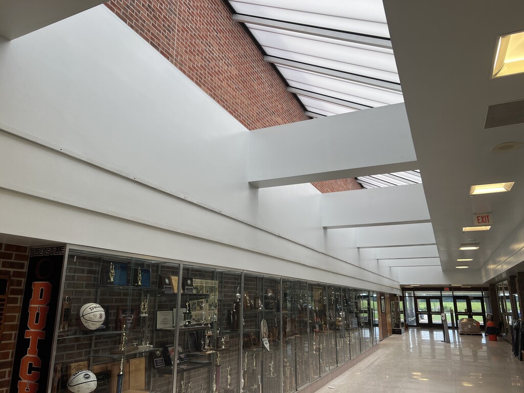 Interior of a school hallway with a white ceiling, brick wall, and glass cases displaying sports items.