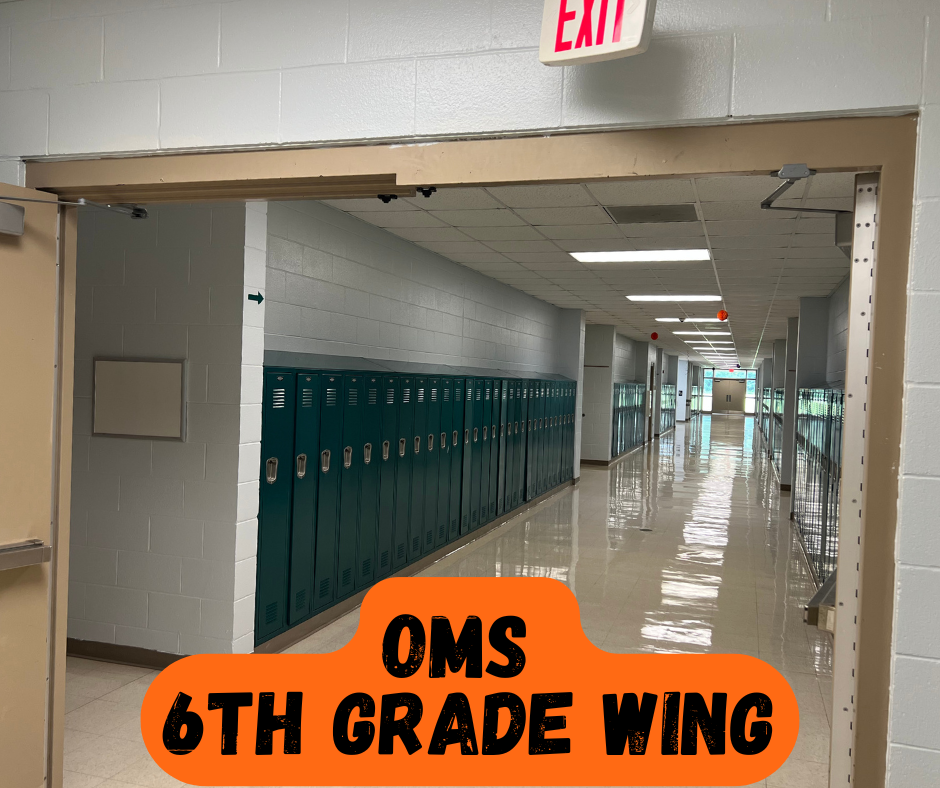 An empty school hallway with lockers on the left and a door open to another hallway.