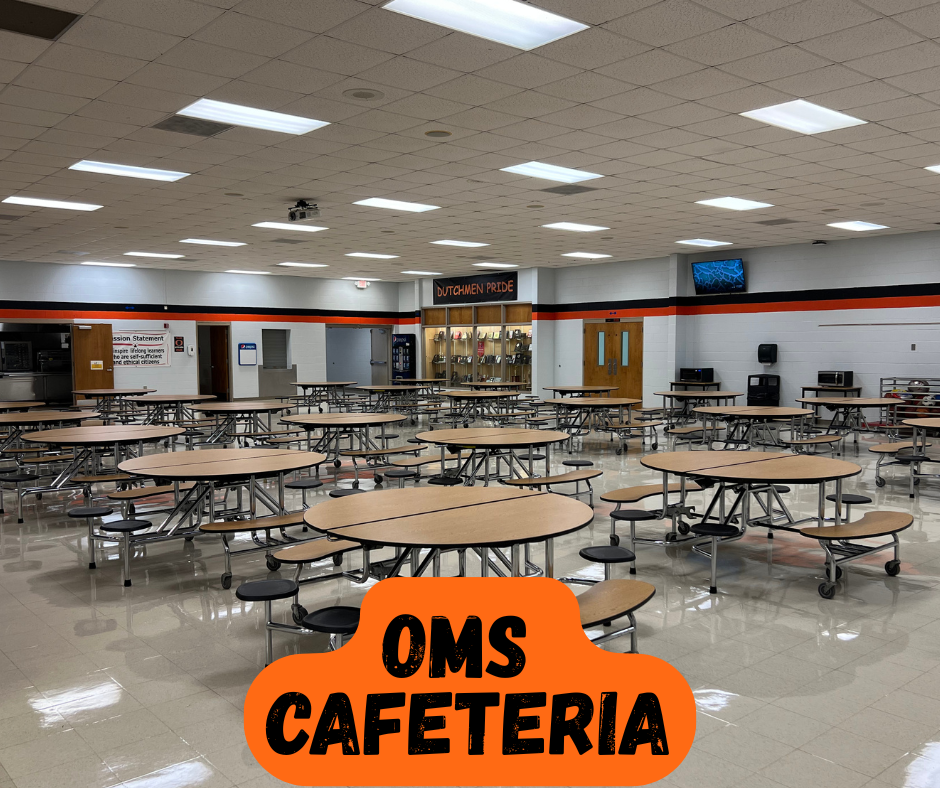 Empty cafeteria with round tables, metal benches, and overhead lighting. An overhead sign reads "OMS CAFETERIA".