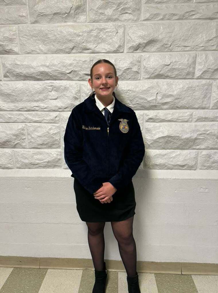 Woman in school uniform stands in front of a textured white stone wall with a checkered floor.