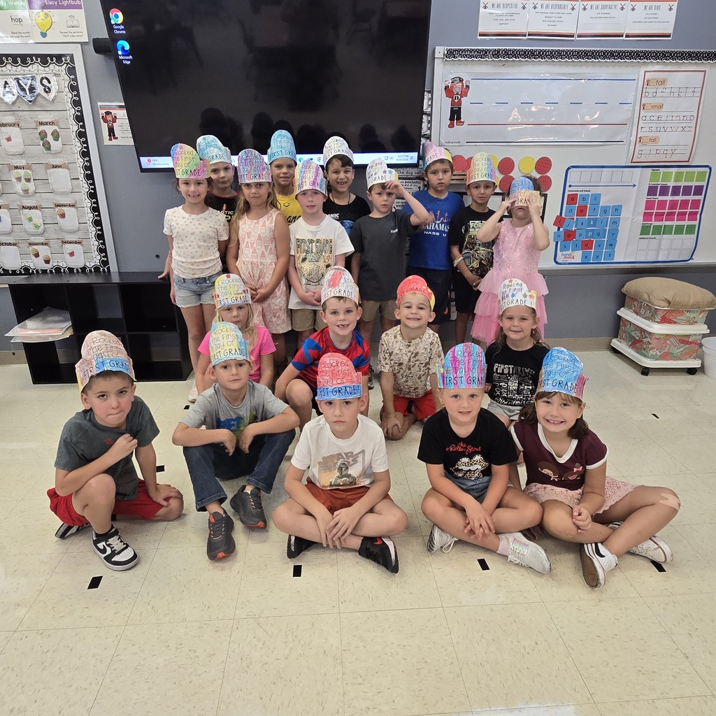 A group of children in hats pose for a picture in a classroom with a large screen.