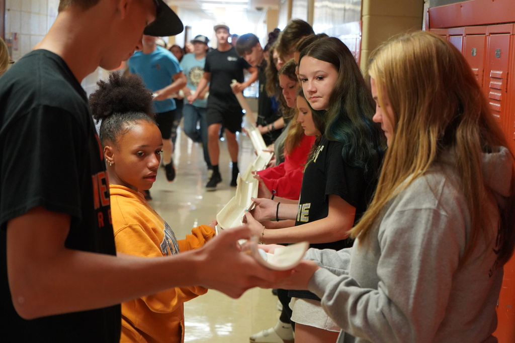 Students in a hallway, with one person holding a large shell, and another person holding a smaller one.