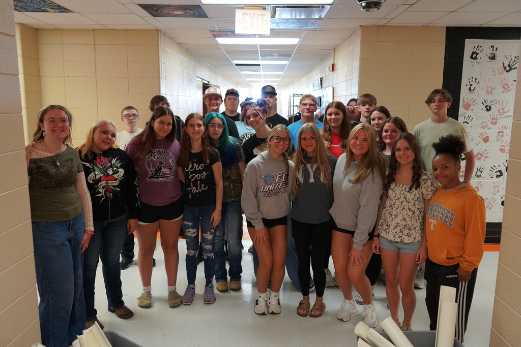 A group of students stand in a hallway with yellow walls, smiling for a photo.