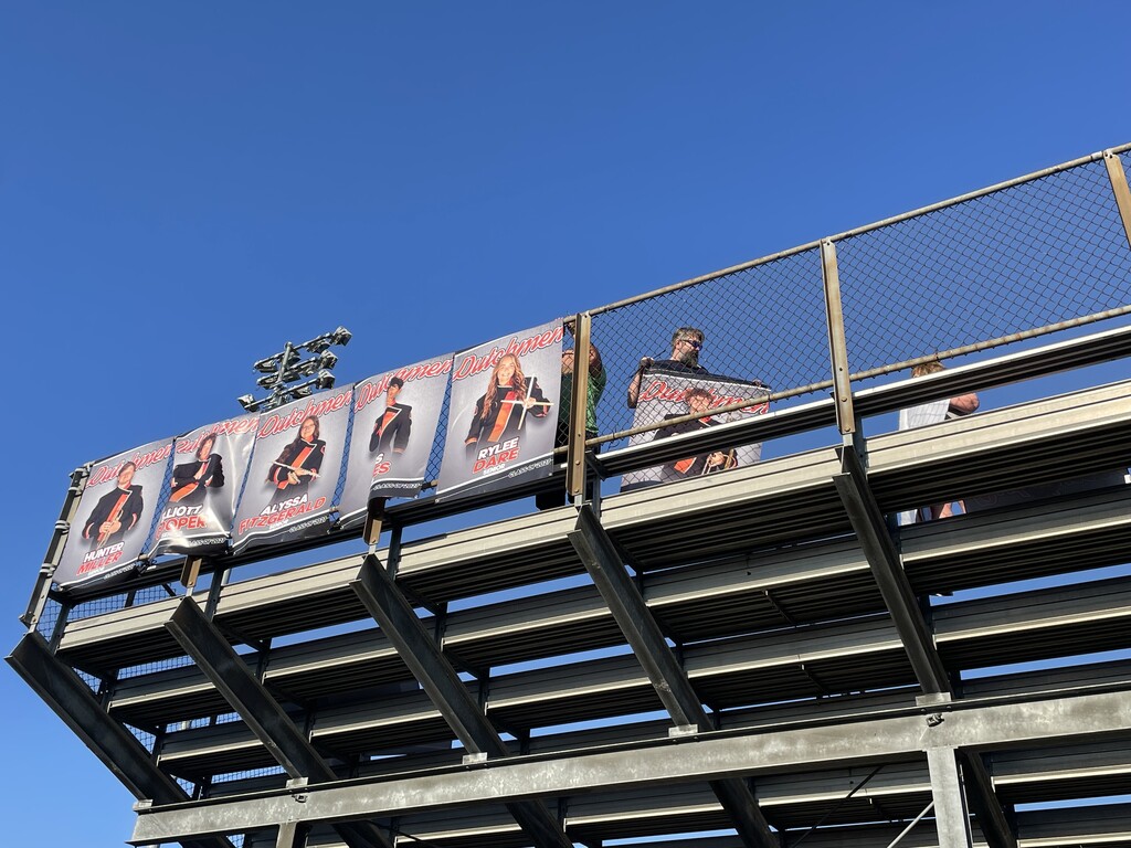 Bleachers with banners, one showing a person, and another showing three people, under a clear blue sky.