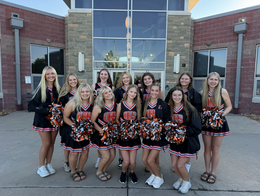 A group of cheerleaders in matching uniforms poses in front of a building with glass windows.