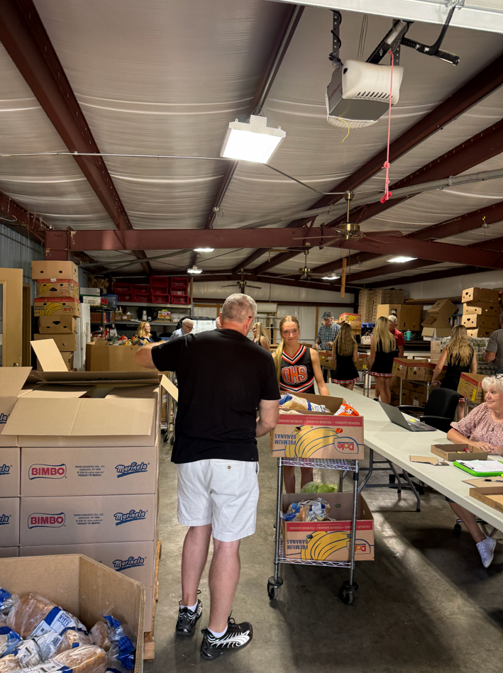 A man in black shirt and white shorts is standing in a warehouse filled with boxes.