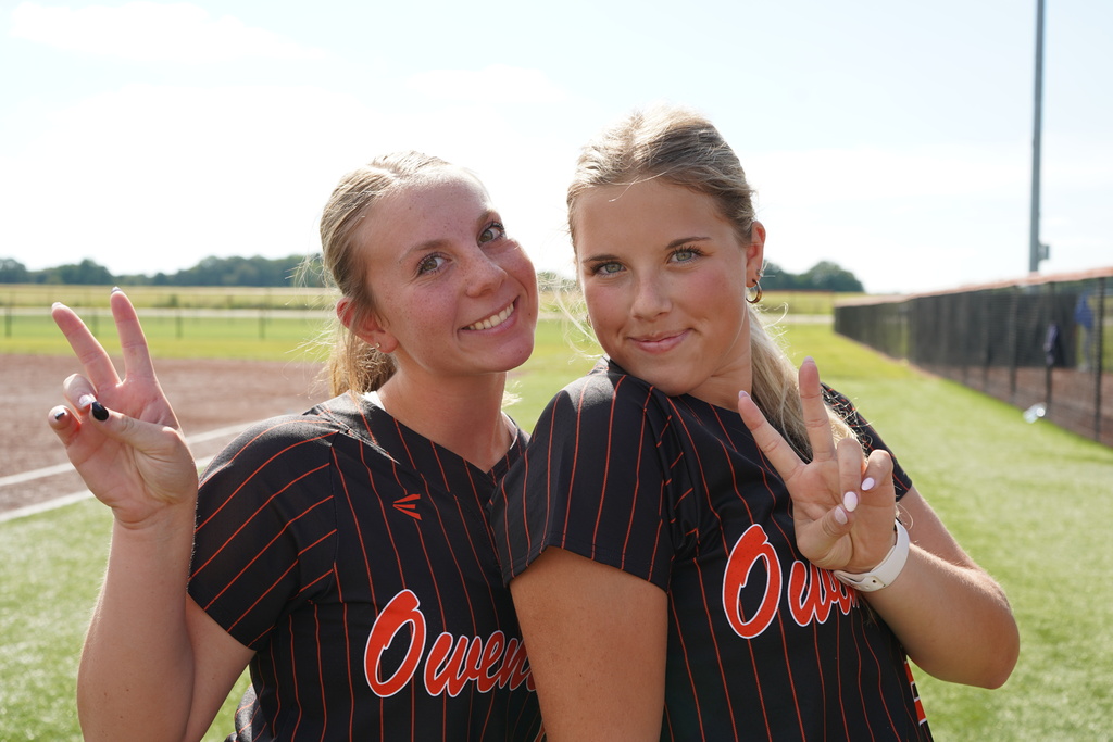 Two women wearing black striped jerseys with "Ove" on the front, smiling and making peace signs.