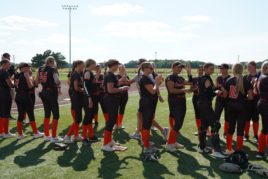 A group of female athletes in matching black uniforms, standing on a field with shadows cast.