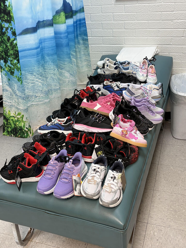 Multiple pairs of sneakers and running shoes on a bench. Background includes a curtain.