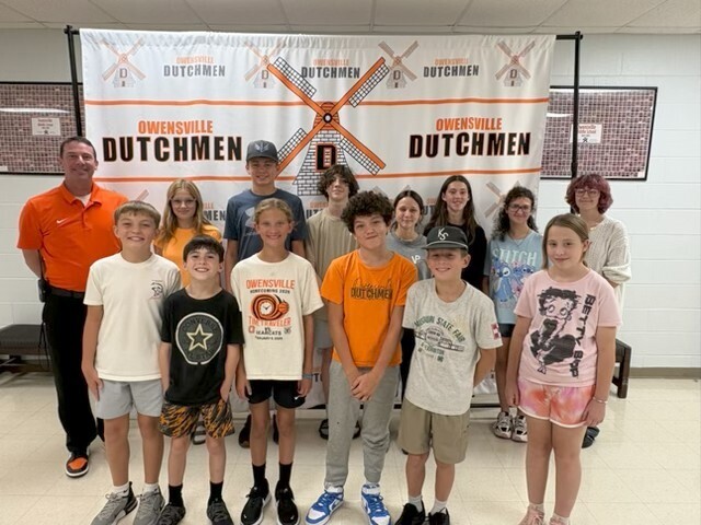 A group of children and adults stand together in front of a banner that reads "DUTCHMEN".