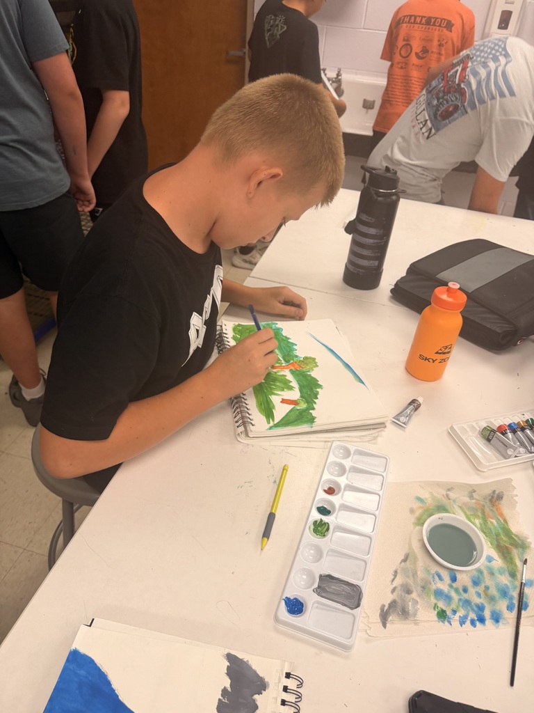 A young person in a black shirt paints a turtle on a canvas at a white table.