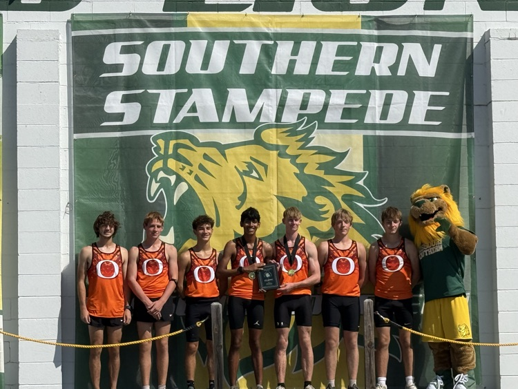 Six athletes and a mascot stand before a banner with "Southern Stampede" and a lion logo. They wear orange jerseys and hold medals.