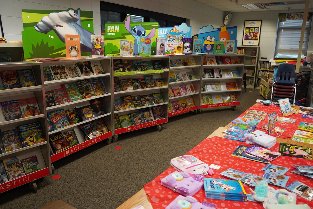 A library filled with children's books on shelves, including a table with colorful items on a red tablecloth.