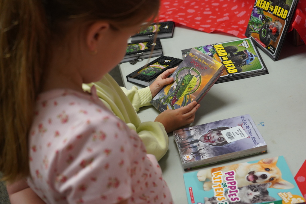 A child wearing pajamas selects a book from a table with several books. Some books have animal illustrations.