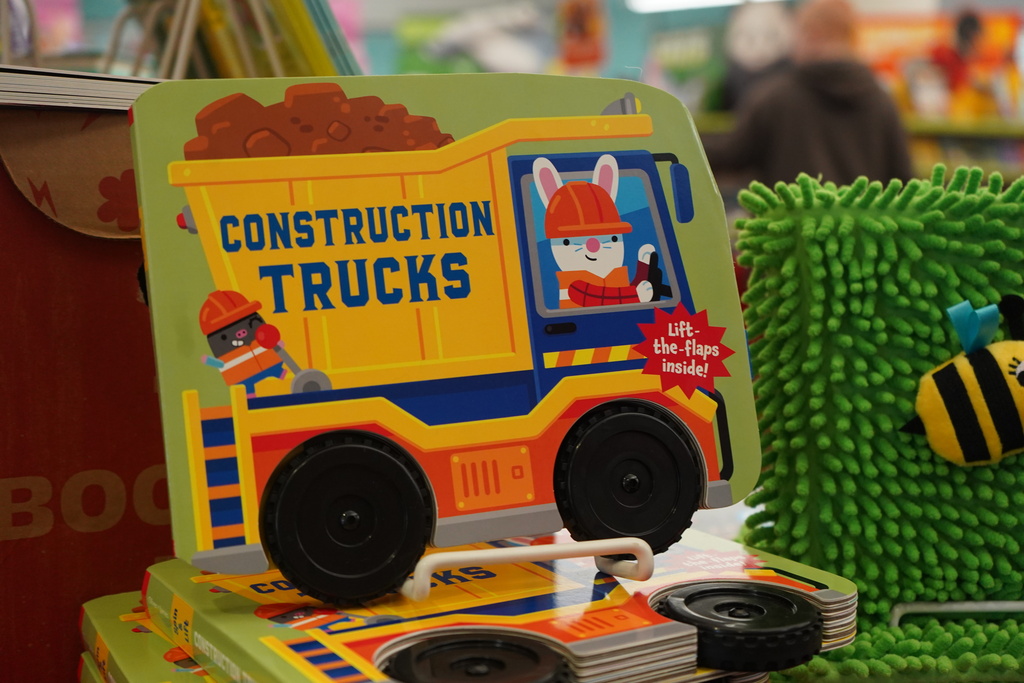 A children's book about construction trucks, featuring a dump truck, displayed next to a bee plush in a store.