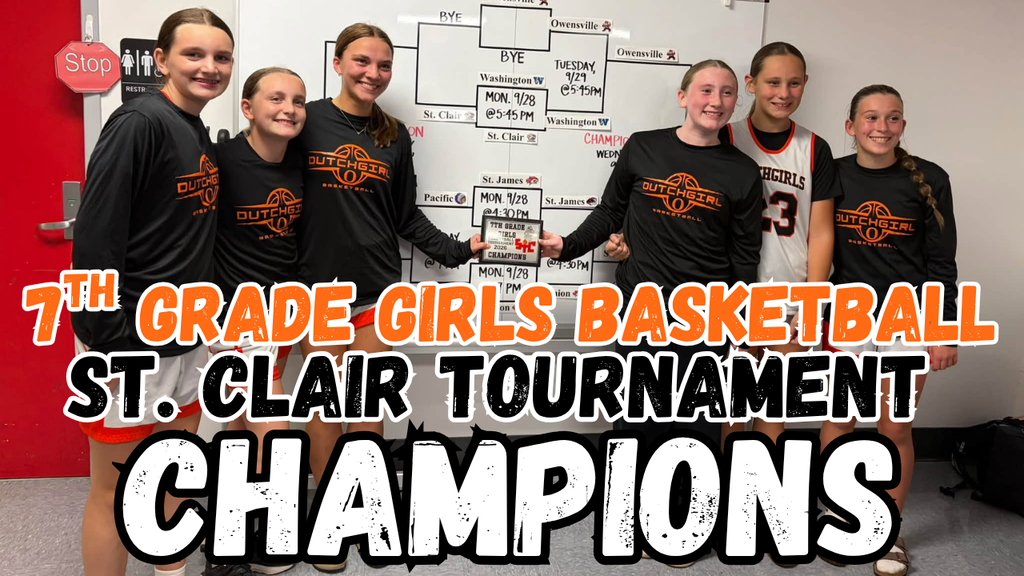 Girls basketball team stands in front of a tournament bracket. They wear matching black shirts with orange and white writing.