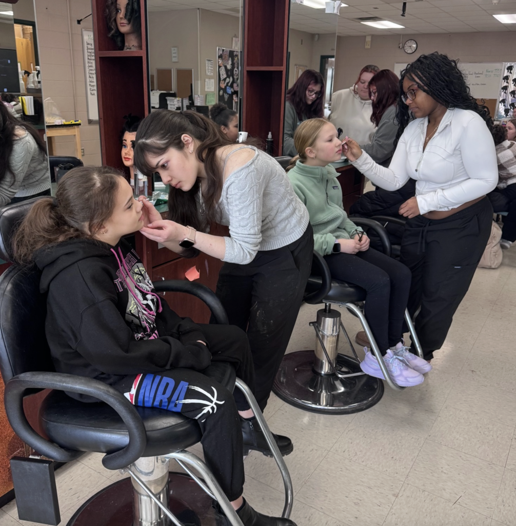 Two students in the Cosmetology program are applying face paint to two visiting students in 4th grade.