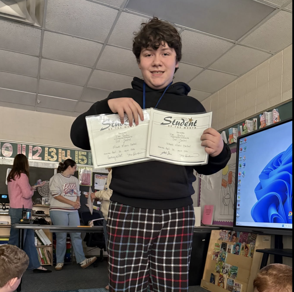 A student is smiling happy to hold up his student of the month certificate.  