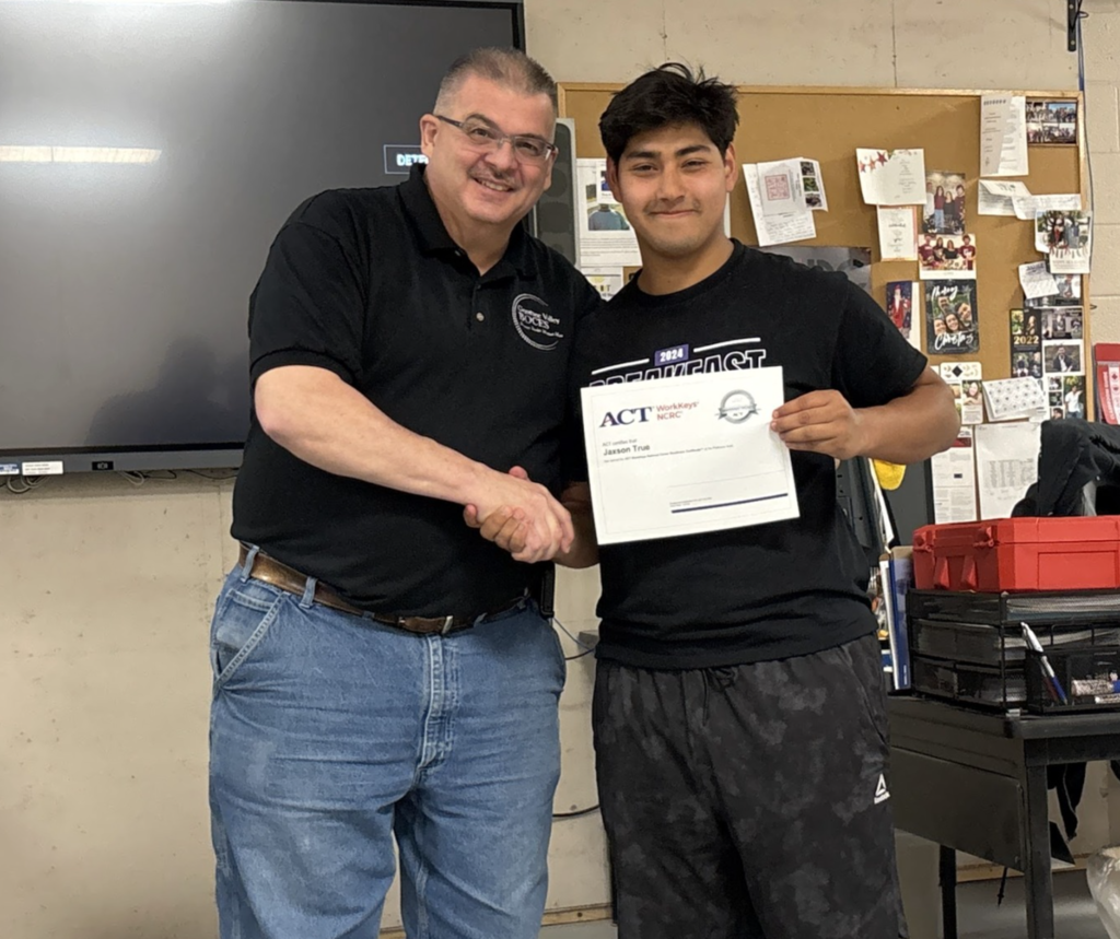 Teacher shaking the hand of his student who holds up is certification.  