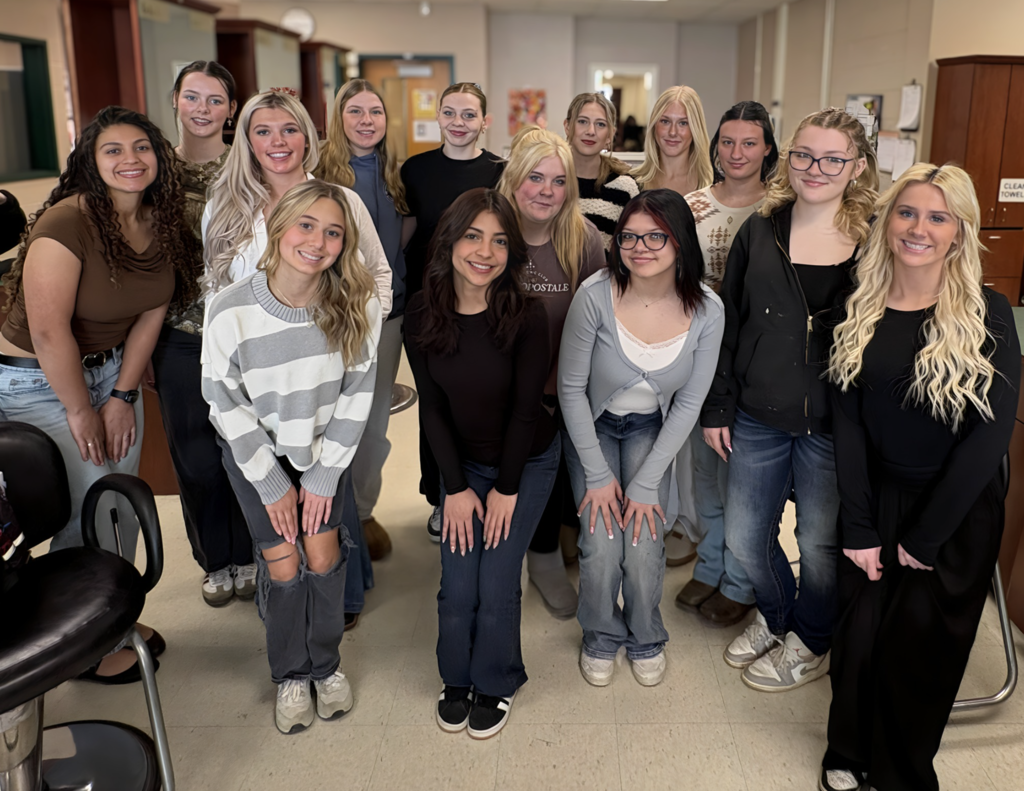 14 students in the classroom salon posing for a picture to celebrate the hours they completed before graduation. They are happy and proud with smiles on their faces.