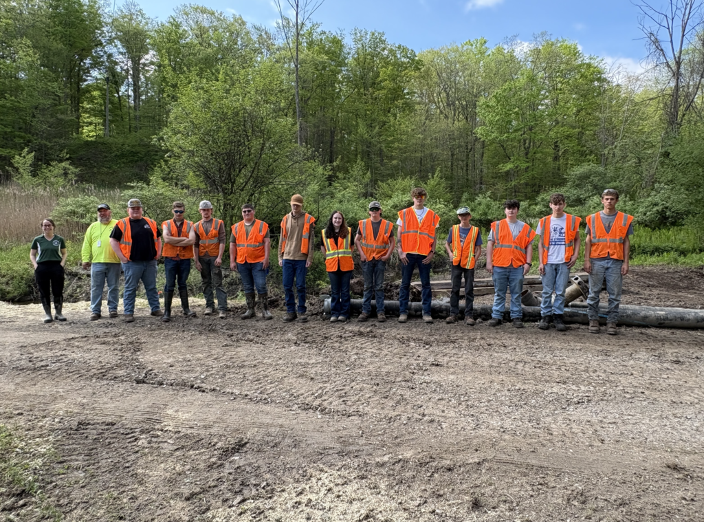 A large group of students and educators standing in front of Black Creek showing off all the work they have done to restore it.