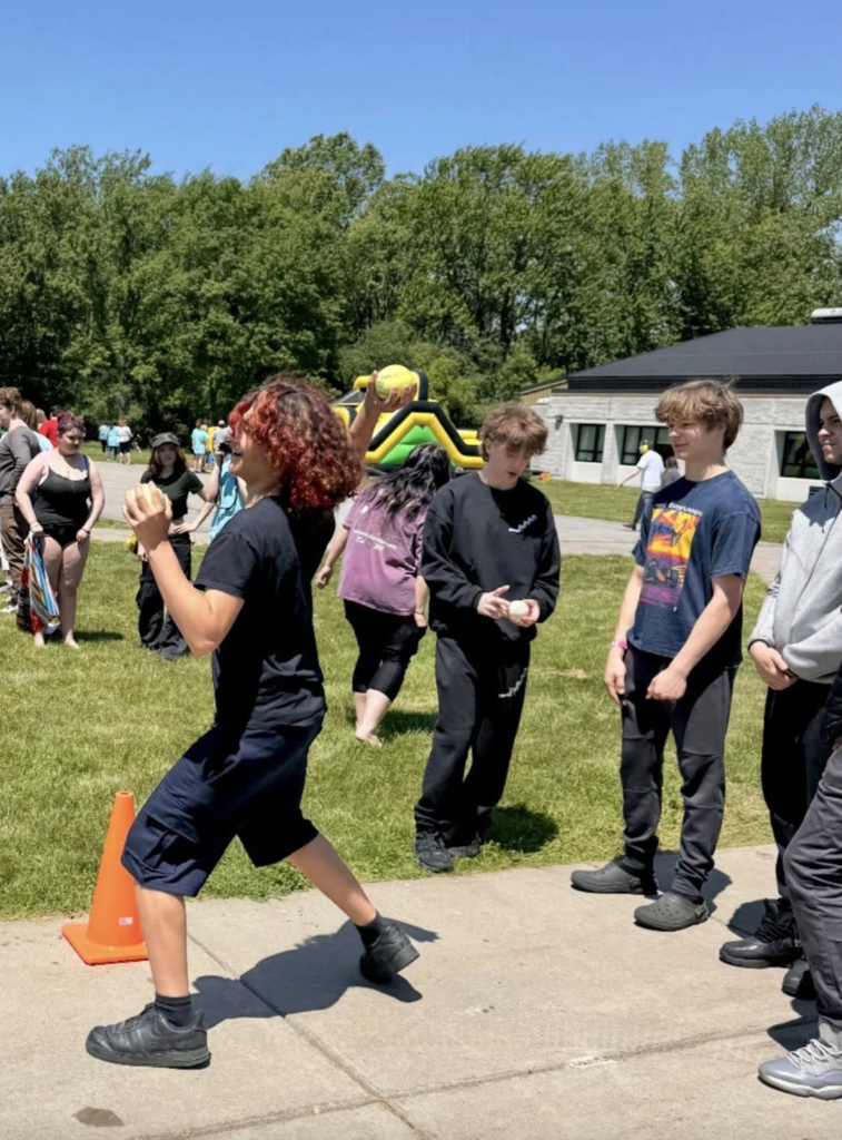 A student takes aim as part  in the dunk tank game by throwinfg the ball at the target while classmates gather nearby to watch and cheer them on.