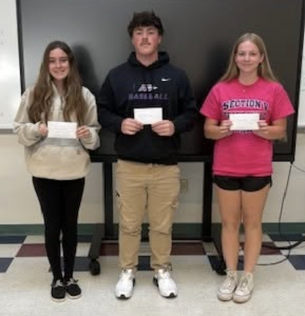 Three students pose with scholarship checks after being selected as scholarship recipients. Their awards recognize their hard work, achievements, and contributions throughout the school year.