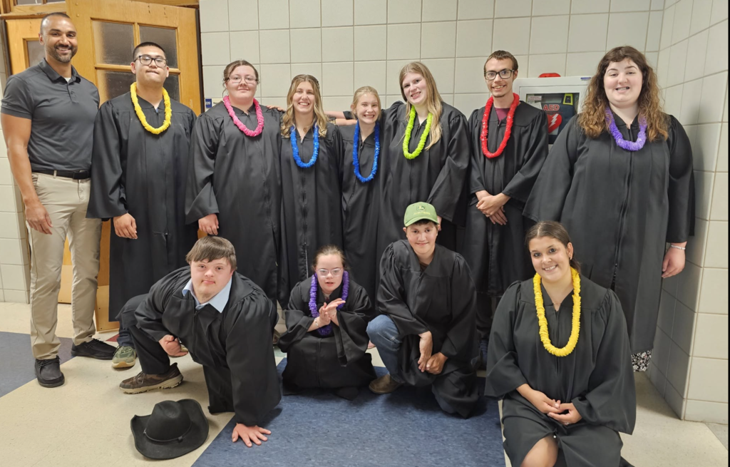 Dansville students gather for a group photo in their graduation gowns before their Moving On Ceremony. Wearing colorful leis and smiling alongside staff, the students celebrate an important milestone as they prepare for their next chapter.