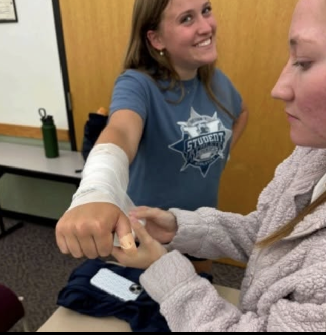 A student demonstrates her first aid skills by applying a bandage to a classmate's hand during a competition. The hands-on activity allowed her to practice proper wrapping techniques and showcase the skills she has learned.