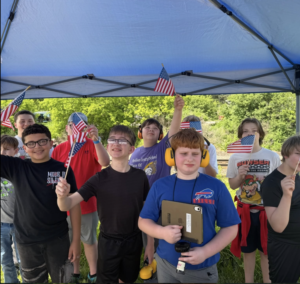 A group of students standing under a tent with American Flags in hand smiling and excited.  