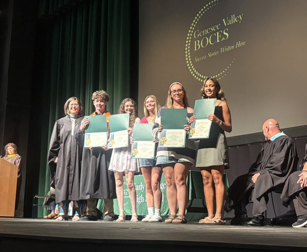 Five students stand on stage holding up an award during the end of year event. 