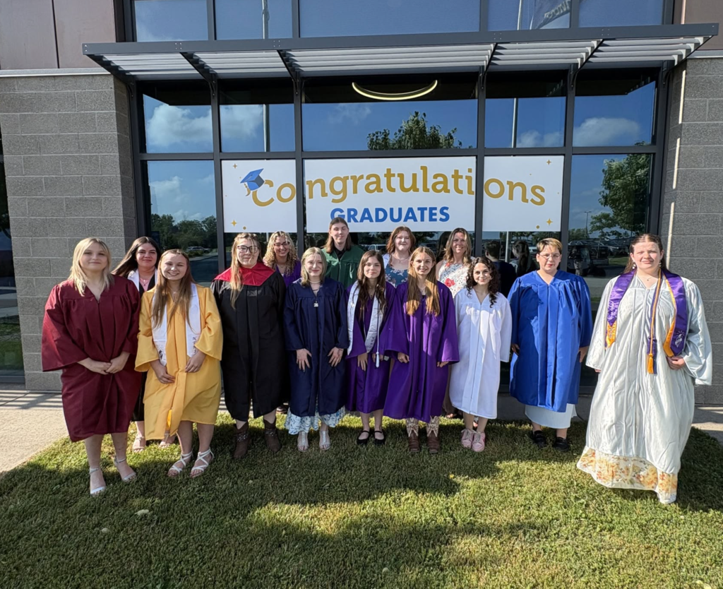 A group of students standing outside in front of a congratulations graduates sign. 
