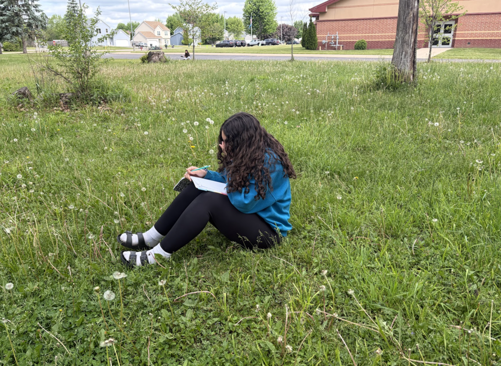 7th grade ELA students took advantage of the beautiful weather today by bringing their creative writing outdoors. As part of their current creative writing unit, students focused on developing strong setting and imagery by paying close attention to the world around them, what they could see, hear, smell, and feel in nature. Using the outdoors as inspiration, students worked to create vivid descriptions that help bring their writing to life. 7