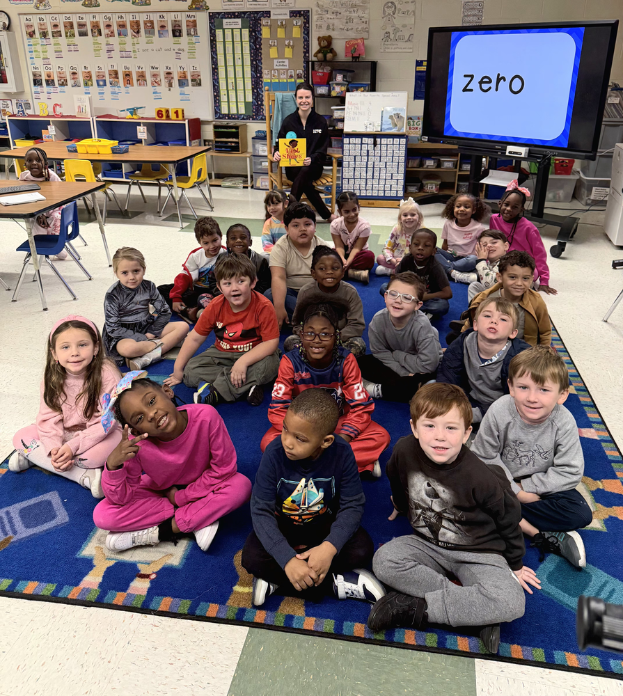 Kindergarten students sitting on rug with guest reader 