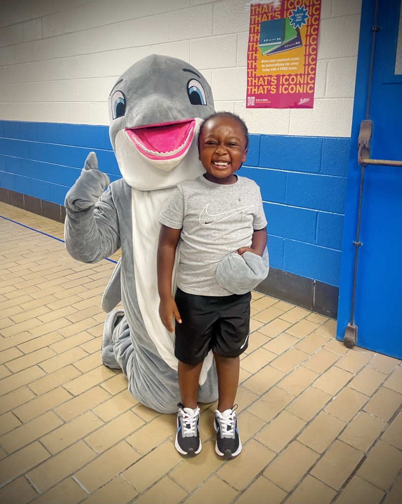 A young african american boy smiling while a dolphin mascot kneels behind him with a thumbs up