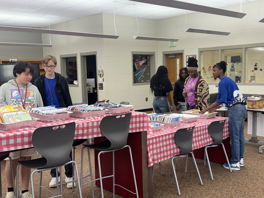 Students standing at table looking through books.
