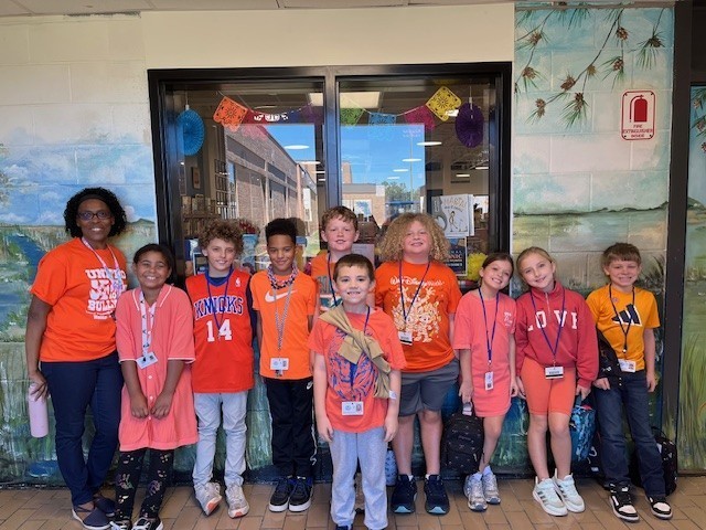 Boys & Girls standing together, most wearing the color orange. 