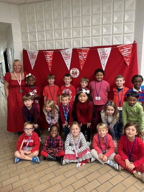 A group of young students dressed in red pose in front of a red backdrop decorated with “Be Drug Free” and “Celebrate Red Ribbon Week” banners. The children smile and hold props supporting Red Ribbon Week’s drug-free message.