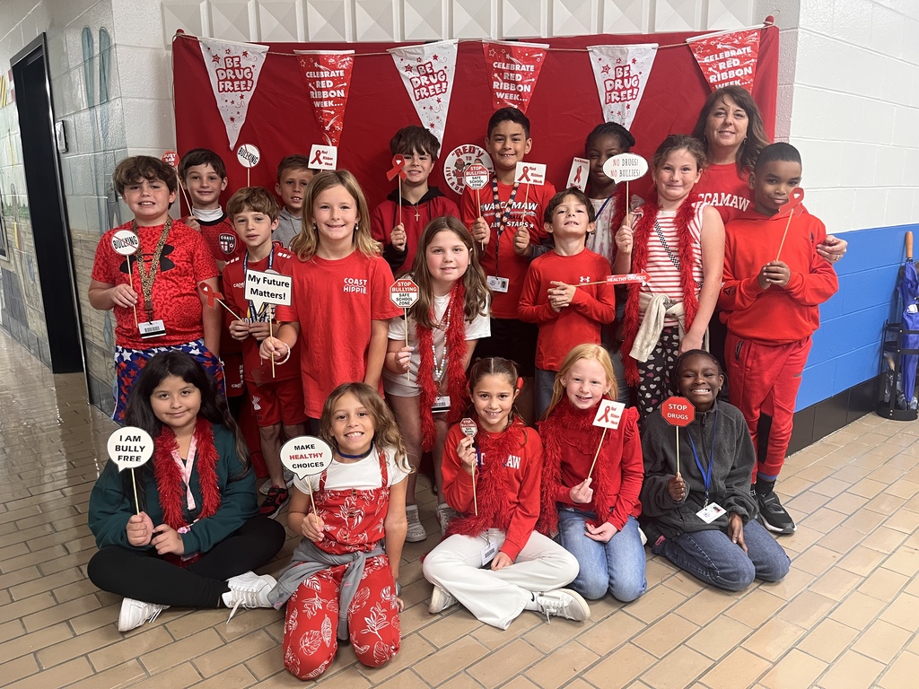 A group of young students dressed in red pose in front of a red backdrop decorated with “Be Drug Free” and “Celebrate Red Ribbon Week” banners. The children smile and hold props supporting Red Ribbon Week’s drug-free message.