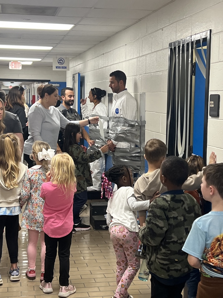 Students line up in the hallway watching as teachers and staff help tape two adults to the wall with silver duct tape.